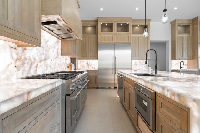 kitchen with high end appliances, decorative light fixtures, custom range hood, sink, and light stone counters