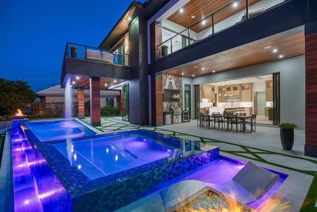 pool at night with a patio, an in ground hot tub, and pool water feature