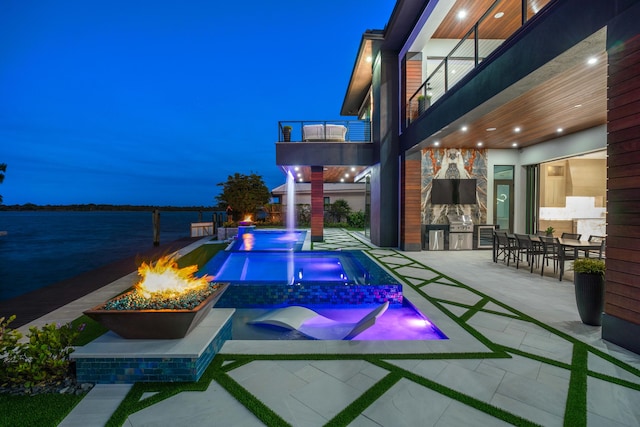 pool at twilight featuring an outdoor fire pit, an in ground hot tub, a patio, and a water view