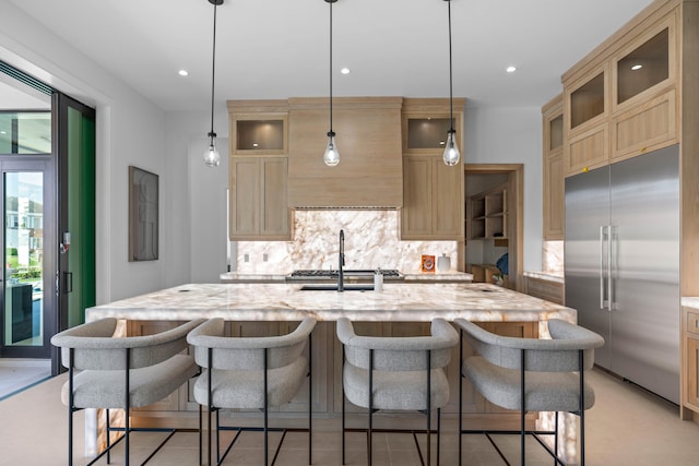 kitchen with hanging light fixtures, built in refrigerator, an island with sink, and tasteful backsplash