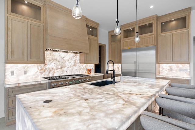 kitchen with decorative light fixtures, appliances with stainless steel finishes, custom exhaust hood, sink, and a kitchen island with sink