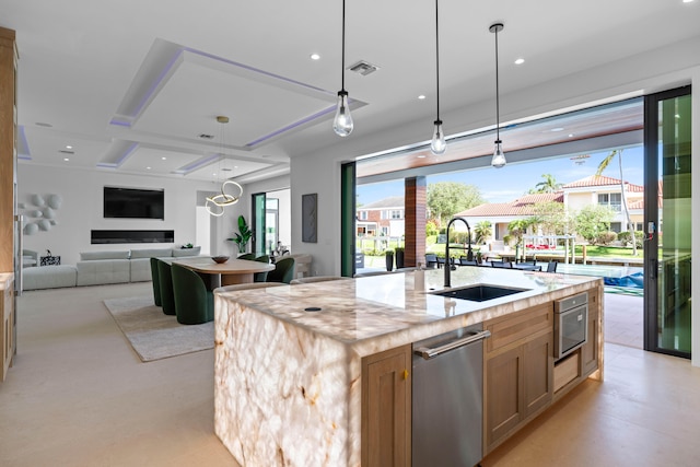 kitchen with decorative light fixtures, light stone countertops, stainless steel appliances, sink, and an island with sink