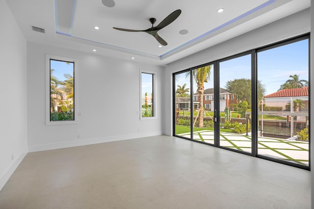 empty room featuring a tray ceiling, concrete flooring, and ceiling fan