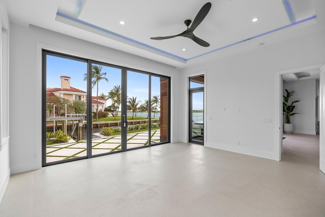 empty room featuring a tray ceiling, a water view, concrete flooring, and ceiling fan