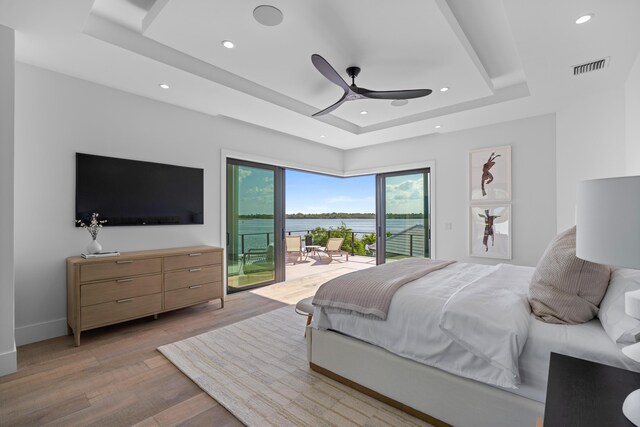 bedroom featuring light wood-type flooring, ceiling fan, a raised ceiling, and access to exterior