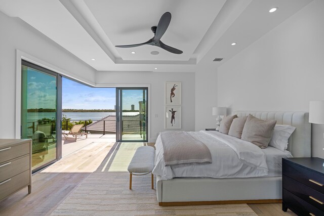 bedroom with light hardwood / wood-style flooring, ceiling fan, a water view, and access to outside