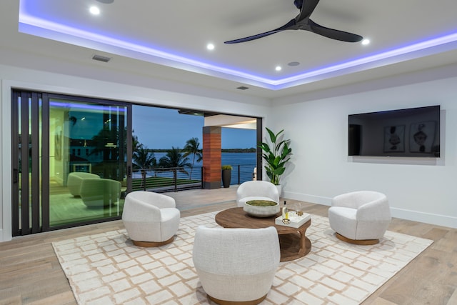 living area featuring a raised ceiling, hardwood / wood-style floors, and ceiling fan