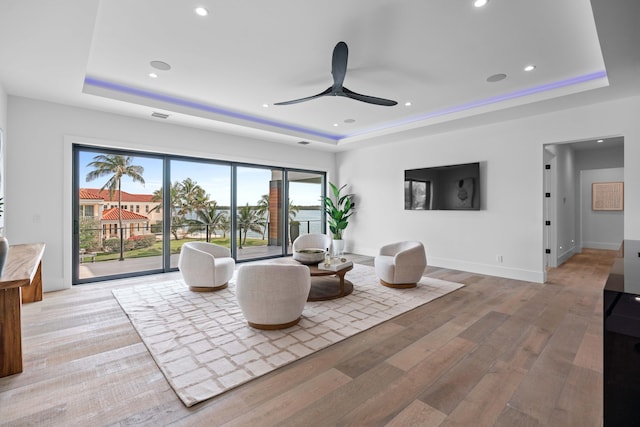 living room with ceiling fan, hardwood / wood-style floors, and a tray ceiling