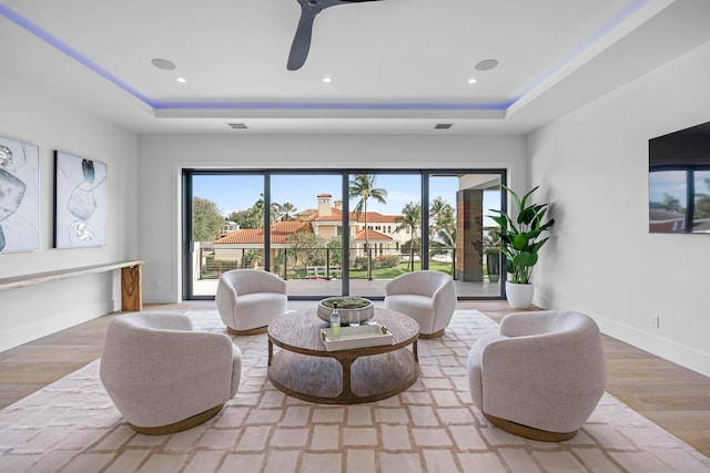 living room featuring ceiling fan, a raised ceiling, and light hardwood / wood-style floors