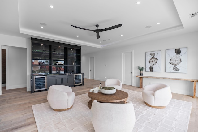 living room featuring bar, a tray ceiling, light hardwood / wood-style floors, and beverage cooler