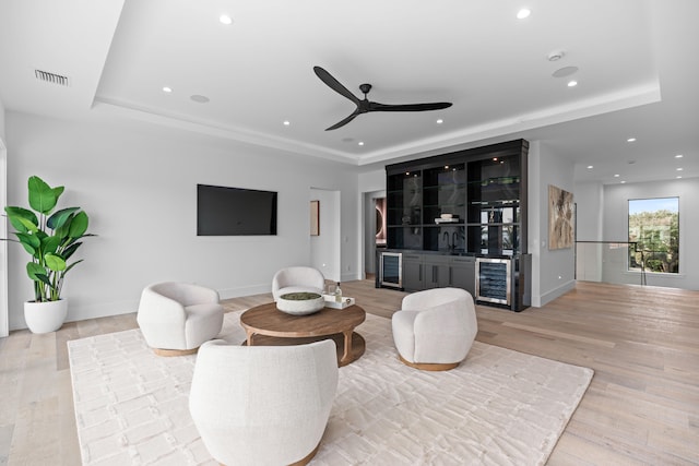 living room with a raised ceiling, indoor wet bar, beverage cooler, and light wood-type flooring