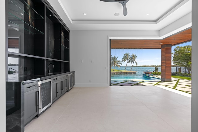 unfurnished living room featuring a raised ceiling, wine cooler, sink, ceiling fan, and a water view