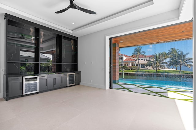 unfurnished living room featuring beverage cooler, ceiling fan, and a raised ceiling