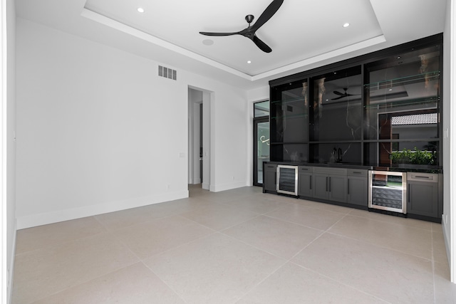 bar featuring beverage cooler, a tray ceiling, and ceiling fan