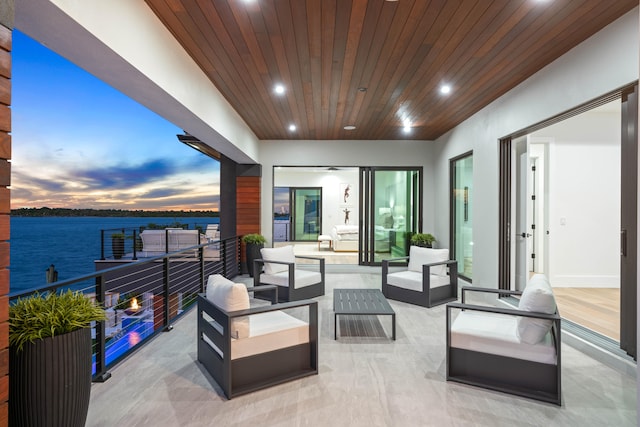 patio terrace at dusk featuring a balcony, an outdoor hangout area, and a water view