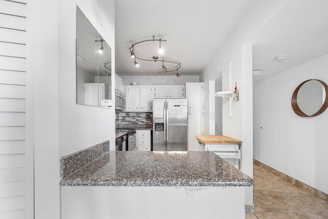 kitchen with decorative backsplash, kitchen peninsula, dark stone counters, white cabinets, and appliances with stainless steel finishes