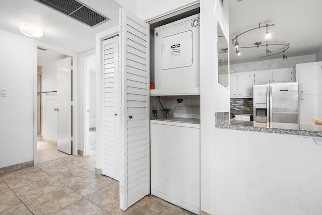 laundry area with stacked washer and dryer and light tile patterned floors