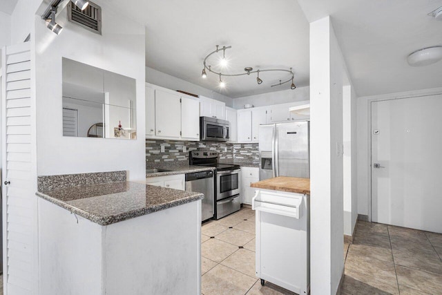 kitchen with appliances with stainless steel finishes, white cabinets, dark stone counters, and backsplash