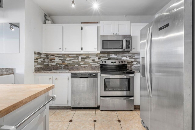 kitchen with backsplash, appliances with stainless steel finishes, white cabinetry, light tile patterned flooring, and sink