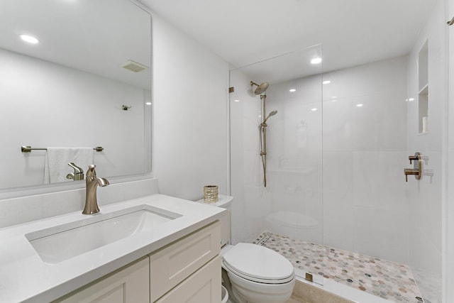 bathroom featuring a tile shower, vanity, and toilet