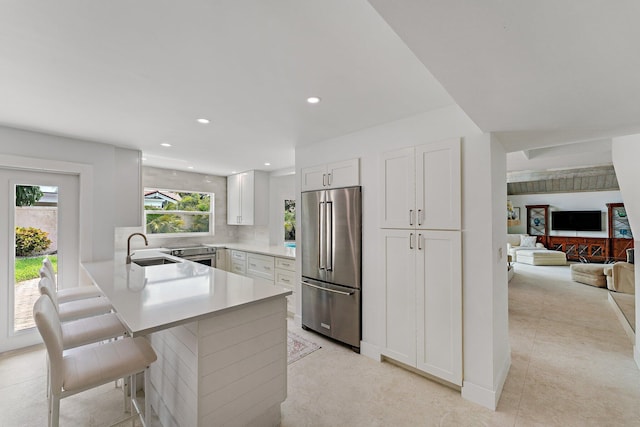 kitchen with white cabinetry, sink, high end refrigerator, kitchen peninsula, and a breakfast bar area