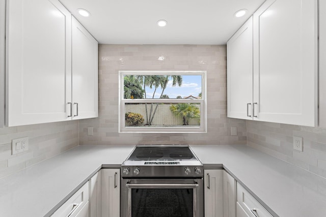 kitchen featuring decorative backsplash, white cabinets, and stainless steel range with electric stovetop