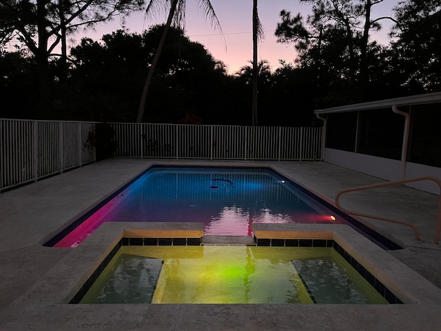 pool at dusk with a patio area and an in ground hot tub