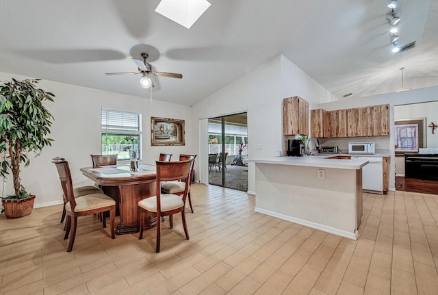 dining space with ceiling fan, vaulted ceiling with skylight, and light hardwood / wood-style floors