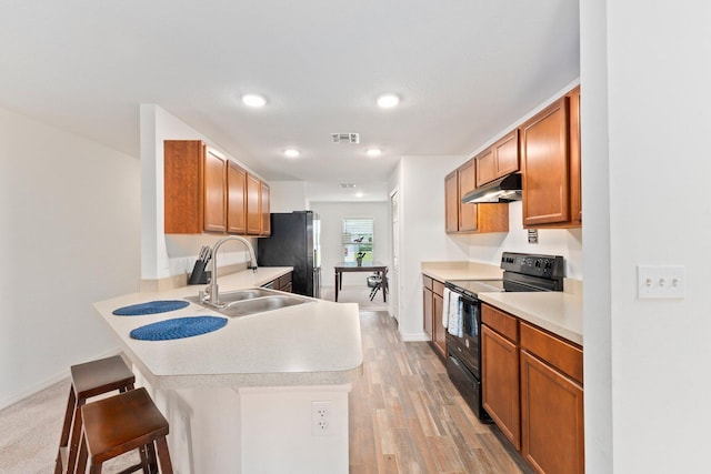 kitchen featuring sink, kitchen peninsula, black appliances, a kitchen breakfast bar, and light wood-type flooring