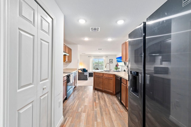 kitchen with light wood-type flooring, black appliances, kitchen peninsula, and sink