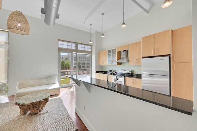 kitchen with wall chimney exhaust hood, appliances with stainless steel finishes, dark stone counters, and pendant lighting