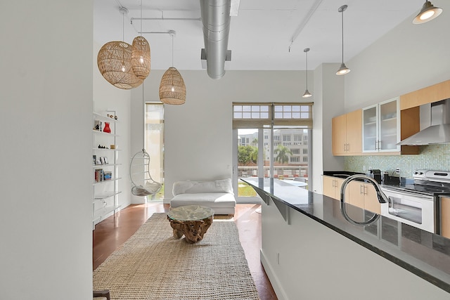 kitchen with a high ceiling, tasteful backsplash, electric range oven, dark wood-type flooring, and wall chimney exhaust hood