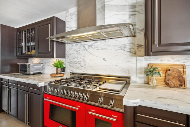 kitchen featuring a toaster, tasteful backsplash, glass insert cabinets, double oven range, and wall chimney exhaust hood