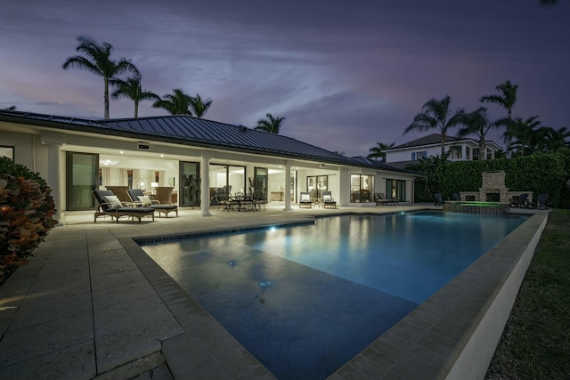 pool at dusk with an outdoor living space with a fireplace and a patio area