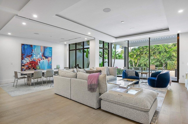 living room with a tray ceiling, recessed lighting, light wood-style floors, a wall of windows, and baseboards