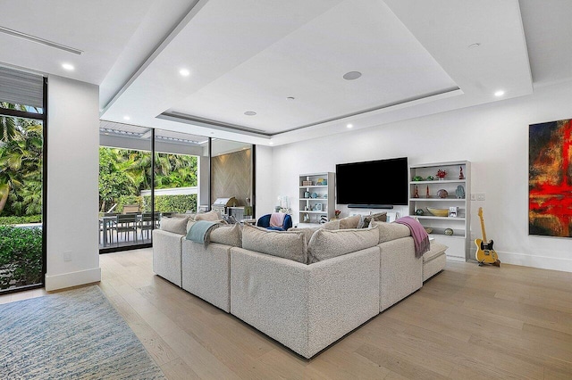 living area with a wall of windows, a tray ceiling, baseboards, and light wood finished floors