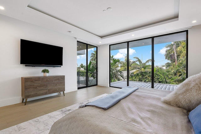 bedroom featuring a wall of windows, access to outside, a raised ceiling, and wood finished floors