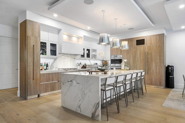 kitchen with a kitchen breakfast bar, light wood-type flooring, white cabinetry, and a large island with sink