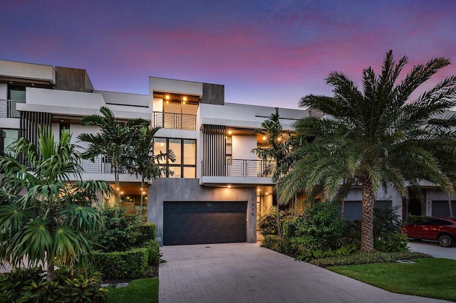 contemporary home with decorative driveway, an attached garage, a balcony, and stucco siding