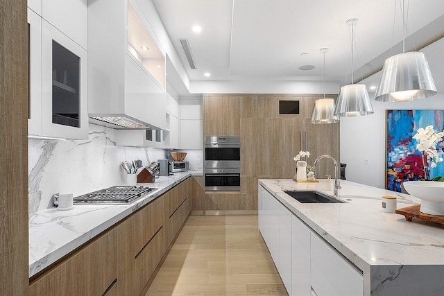 kitchen featuring a sink, white cabinets, wall chimney range hood, appliances with stainless steel finishes, and modern cabinets