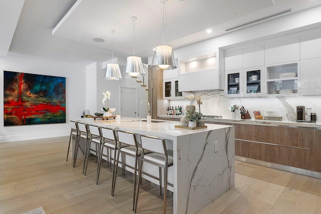 kitchen with a sink, a kitchen breakfast bar, backsplash, light wood finished floors, and modern cabinets