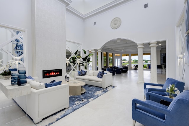 living room featuring ceiling fan, a towering ceiling, a fireplace, light tile patterned floors, and decorative columns