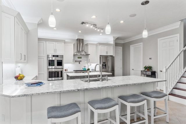 kitchen with pendant lighting, sink, wall chimney exhaust hood, white cabinetry, and appliances with stainless steel finishes