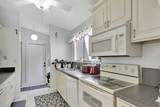 kitchen featuring white appliances, lofted ceiling, a sink, dark countertops, and cream cabinets