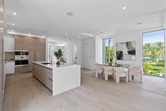 kitchen featuring a center island with sink, light wood-type flooring, sink, and multiple ovens