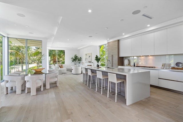 kitchen featuring tasteful backsplash, a kitchen breakfast bar, light hardwood / wood-style flooring, a center island with sink, and white cabinets