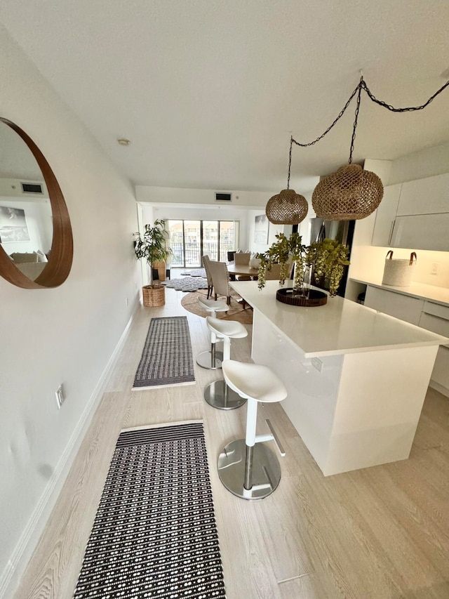 kitchen with a kitchen island, white cabinetry, light hardwood / wood-style flooring, and pendant lighting