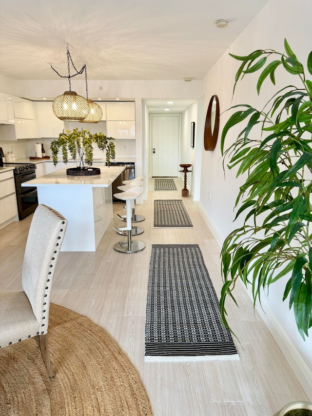 interior space featuring a kitchen breakfast bar, hanging light fixtures, a center island, electric range, and white cabinetry