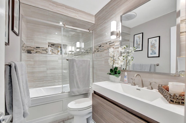 full bathroom featuring vanity, tile walls, combined bath / shower with glass door, toilet, and backsplash