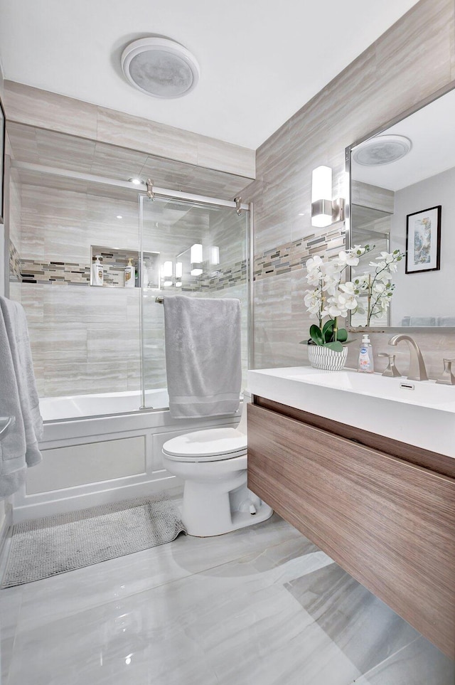 full bathroom with toilet, combined bath / shower with glass door, tile walls, and vanity